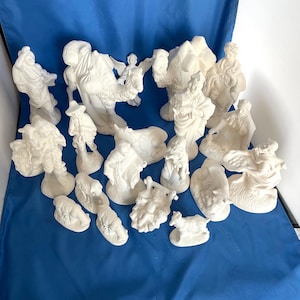 May include: A white ceramic nativity scene set with 18 pieces, including figures of Mary, Joseph, baby Jesus, shepherds, angels, animals, and a camel.