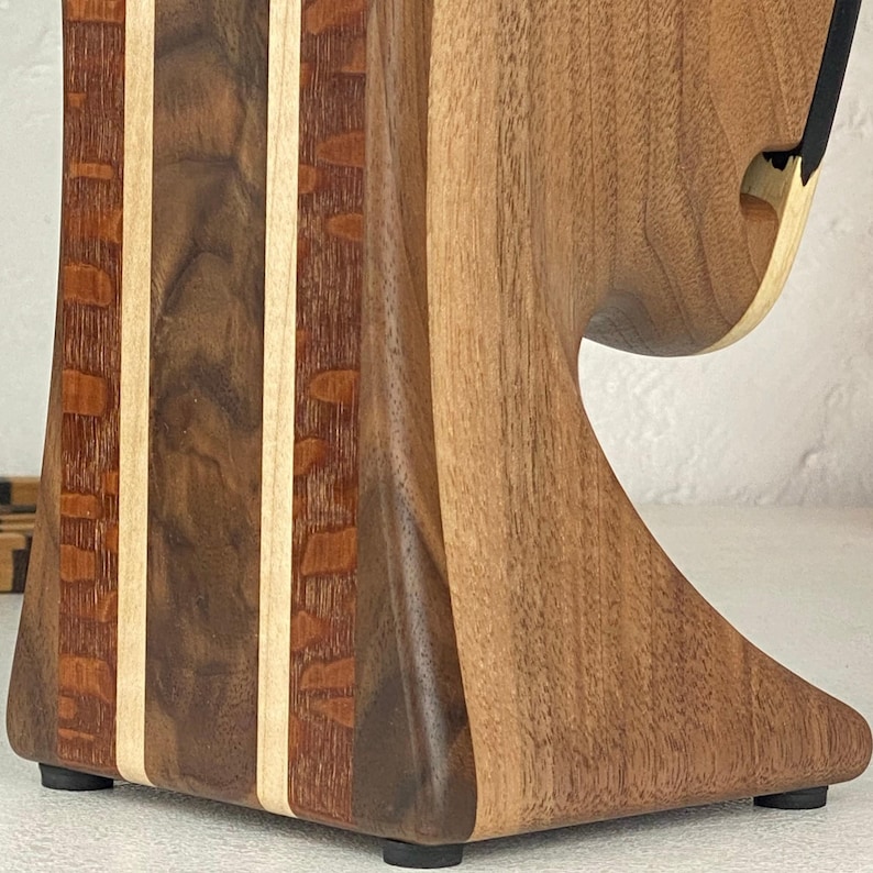 May include: A wooden stand featuring a vertical design with alternating light and dark wood grain patterns. The structure includes two thin, light-coloured vertical strips separating darker, textured wood sections, with a curved cutout.