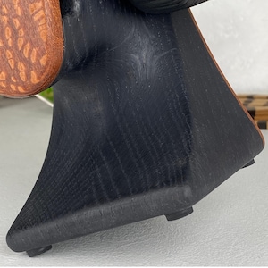 Op de afbeelding: Een sculpturaal houten object met een centrale zwart gebeitste basis met een opvallende houtnerftextuur. De basis wordt geflankeerd door twee ronde, roodbruine houten panelen met een getextureerd oppervlak, ondersteund door kleine zwarte voetjes.