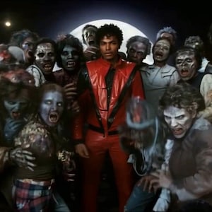 May include: A person wearing a bright red leather jacket with black V-shaped accents and matching red leather trousers, standing in the center of a group of individuals with pale, distressed skin and tattered clothing under a full moon.