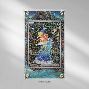 May include: A framed trading card featuring a vibrant illustration of a red and yellow Magikarp leaping from a waterfall. The card is set against a detailed, colorful background with a landscape design. The frame has decorative accents.