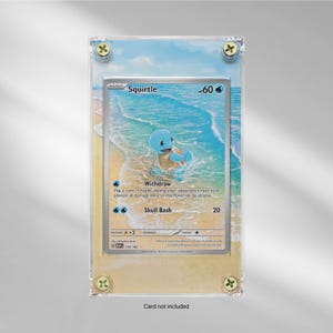 Puede incluir: Una tarjeta coleccionable Pokémon Squirtle enmarcada. La tarjeta presenta un personaje Squirtle azul en una escena de playa. El marco es de acrílico transparente, asegurado con tornillos dorados. El texto "Card not included" está en la parte inferior.
