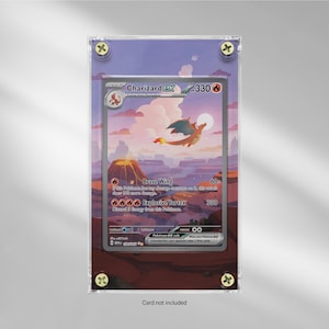 May include: A framed Charizard EX Pokémon card. The card features a fiery orange dragon with blue wings against a sunset landscape. The frame is clear with gold-colored corner screws. The text "Card not included" is at the bottom.