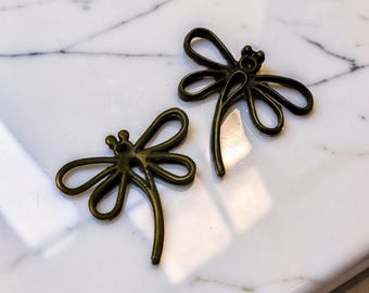 May include: Two bronze-colored dragonfly charms with delicate wing details. The dragonfly charms are made of metal and have a vintage aesthetic. The charms are ideal for jewelry making or craft projects.