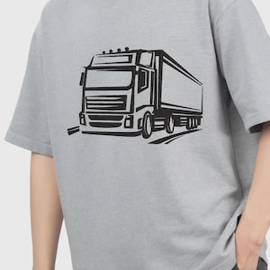 Peut inclure: Un t-shirt gris avec un motif noir d'un camion semi-remorque. Le motif du camion comprend la cabine, la remorque et les roues, avec des détails comme les phares et un porte-bagages. Le t-shirt a des manches courtes et un col rond.