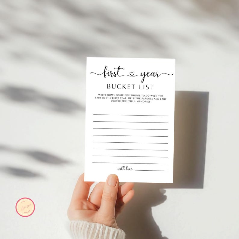 Może przedstawiać: Drukowana karta do gry na baby shower z tekstem "first year bucket list" i instrukcjami, aby zapisać zabawne rzeczy do zrobienia z dzieckiem w pierwszym roku.