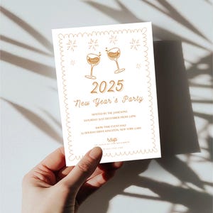 Puede incluir: Una tarjeta de invitaci&oacute;n blanca con un borde dorado y una ilustraci&oacute;n dorada de dos copas de champ&aacute;n con fuegos artificiales. El texto de la tarjeta dice "2025 New Year's Party" e incluye detalles sobre el evento, incluyendo la fecha, la hora, la ubicaci&oacute;n y la informaci&oacute;n de RSVP.