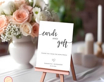 May include: White card with black calligraphy that reads "cards and gift" with a heart and the text "Thank you from the newlyweds Samantha + Alexander 04-09-20XX". The card is on a small wooden easel.