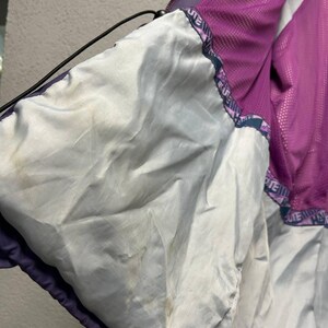 May include: Interior view of a purple and white jacket. The jacket's lining is white, with a purple mesh panel visible. The jacket has a drawstring and a printed border with the word "HATE" repeated. The jacket appears to be worn.