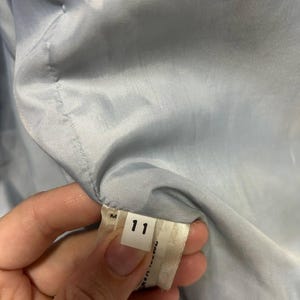 May include: A close-up of a tag with the number 11 printed on it. The tag is white with black text and is attached to a light blue fabric. The fabric is part of a garment.