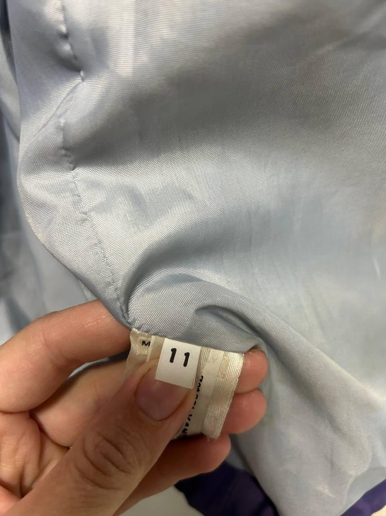 May include: A close-up of a tag with the number 11 printed on it. The tag is white with black text and is attached to a light blue fabric. The fabric is part of a garment.