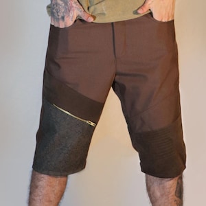 May include: A tan tank top and brown shorts with a gold zipper. The shorts have a dark gray panel on the side and a textured panel on the knee. The outfit is casual and modern.