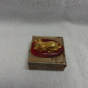 May include: A small, rectangular, metal box with a red interior and a gold-coloured cat figurine on the lid.