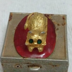 May include: A vintage metal trinket box with a gold cat figurine on the lid. The cat has green gem eyes and is sitting on a red oval.