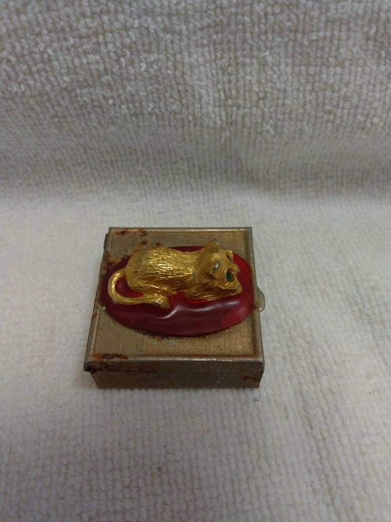 May include: A small, rectangular, metal box with a gold finish. The box has a red and gold lion figurine on the lid.