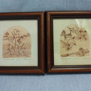 Op de afbeelding: Twee ingelijste prints van botanische illustraties. De linker print toont een bruine lijntekening van een bloeiende plant met de tekst "A Autumn Bell #1765  Rosamond." De rechter print toont een bruine lijntekening van een bloeiende tak met de tekst "Blooming Time #1723 Rosamond."