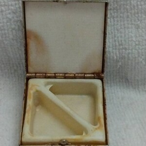 May include: A small, silver-coloured metal box with a hinged lid. The box is divided into two compartments by a diagonal divider. The box is slightly tarnished and has a worn appearance.