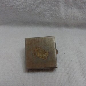 May include: A small, silver, rectangular box with a gold design on the top. The box has a hinged lid and a small latch.