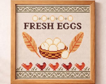May include: Framed cross-stitch artwork with a rustic theme. The design features the text "FRESH EGGS" above a basket of eggs, flanked by feathers. Below are several red chickens. The frame is made of wood.