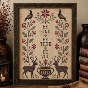 Può includere: Opera d'arte a punto croce incorniciata con le parole "BE KIND BE TRUE BE YOU". Il design presenta uccelli, cervi, elementi floreali e un vaso decorativo nei toni del marrone, rosso e verde. La cornice è marrone scuro.
