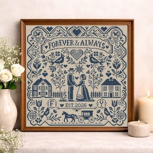 May include: A framed cross-stitch artwork with a brown wooden frame. The design features a couple, houses, birds, and the text "FOREVER & ALWAYS" and "EST. 2026" in navy blue on a beige background. The artwork is a wedding or anniversary theme.