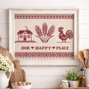 May include: Framed cross-stitch artwork featuring a red house, wheat stalks, and a rooster on a beige background. The text "OUR HAPPY PLACE" is stitched below the images. The frame is white.