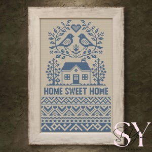 May include: A framed cross-stitch featuring a blue and white design. The artwork depicts two birds above a house with the text "HOME SWEET HOME". The frame is white with a distressed finish, adding a rustic touch to the piece.