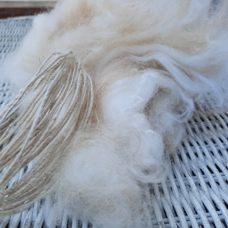May include: A close-up of a pile of white and beige wool fibers, with a bundle of natural twine string visible in the foreground.