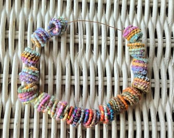May include: A colorful necklace made of fabric scraps, with a variety of colors and patterns. The necklace is strung on a wire and has a variety of shapes and sizes.