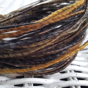 May include: A close-up of a skein of yarn with black, brown, and gold strands. The yarn is soft and fuzzy, and it is perfect for knitting or crocheting.