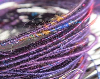 May include: Close-up of a spool of purple yarn with red, blue, and gold accents. The yarn is tightly wound and has a fuzzy texture.