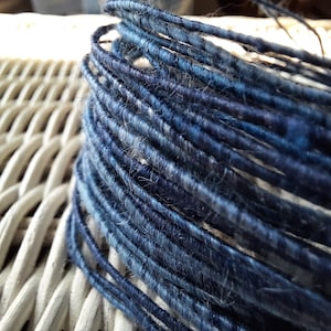 May include: Close-up of a spool of blue and white yarn. The yarn is tightly wound and has a fuzzy texture.