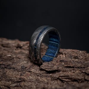 May include: A silver ring with a blue wood inlay. The ring has a hammered finish and a wide band.