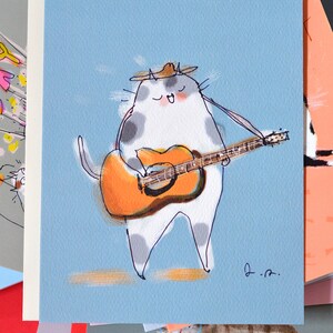 May include: A white cat with gray spots wearing a brown hat plays a brown acoustic guitar. The cat is singing and has its eyes closed. The background is light blue.