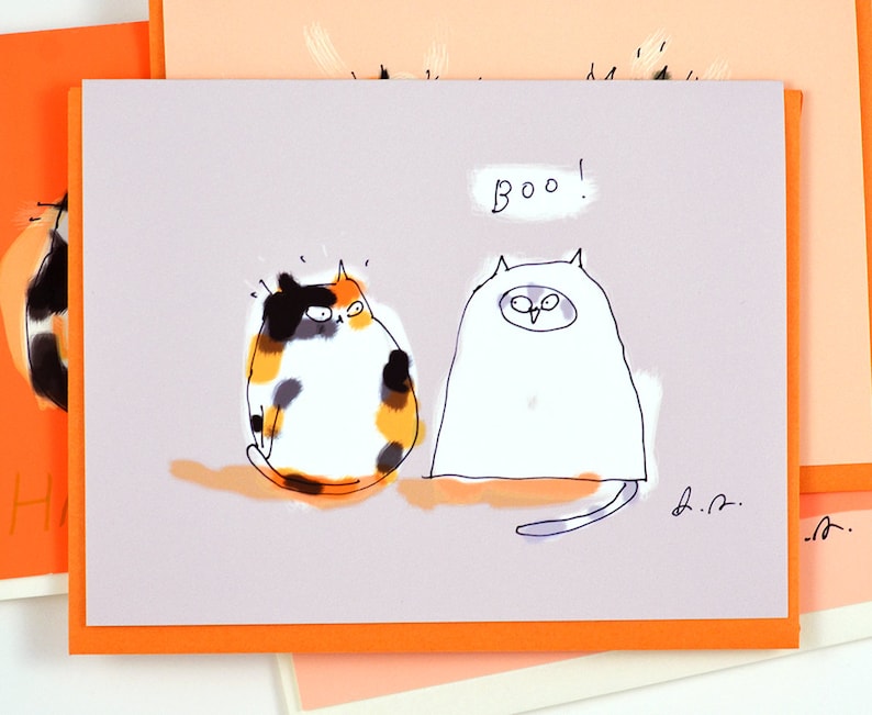 Pu&ograve; includere: Un biglietto d'auguri con uno sfondo viola chiaro che presenta un'illustrazione di due gatti in stile cartone animato. Un gatto indossa un costume da fantasma bianco e l'altro &egrave; un gatto calico. Il testo "Boo!" &egrave; scritto sopra i gatti. Il biglietto ha un bordo arancione.