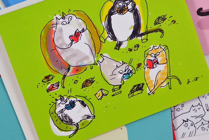 May include: A green card with a hand-drawn illustration of five cats reading books. The cats are sitting in chairs and on the floor. There are small brown and yellow objects scattered around the cats. The card is signed "A.C."