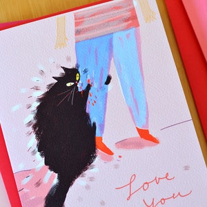 May include: A pink greeting card with a black cat scratching a person's leg. The person is wearing blue pants and red shoes. The card says "love you" in pink cursive writing.
