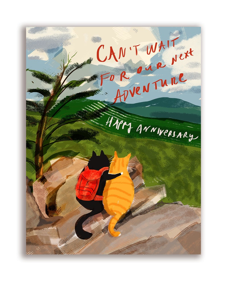 May include: A greeting card with a watercolor illustration of two cats sitting on a rock overlooking a mountain range. The text on the card reads "Can't wait for our next adventure. Happy Anniversary."