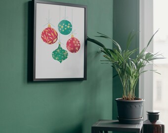 May include: A framed print featuring four Christmas ornaments in red, green, and teal. The ornaments have various patterns, including leaves and stars, and are suspended by thin strings against a white background. The frame is black.