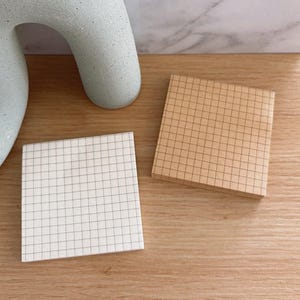 May include: Two square sticky note pads with grid patterns. One pad is white with black grid lines and the other is light brown with brown grid lines.