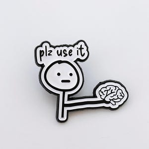 May include: A black and white enamel pin depicting a stick figure with the text "plz use it". The figure is holding a brain. The pin has a glossy finish and is suitable for clothing or bags.
