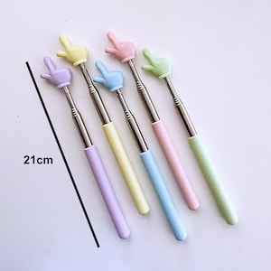 K&ouml;nnte beinhalten: F&uuml;nf farbige, einziehbare Selfie-Sticks mit handf&ouml;rmigen Griffen. Die Sticks sind 53,3 cm lang und in Pink, Hellblau, Gelb, Gr&uuml;n und Lila erh&auml;ltlich.
