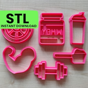 May include: A set of six pink plastic cookie cutters shaped like a dumbbell, a weight plate, a protein shaker, a protein powder container, a bicep, and a scoop. The protein powder container has the word "WHE" printed on it.