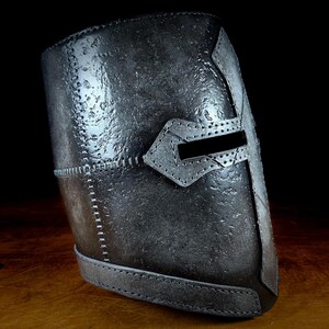 K&ouml;nnte beinhalten: Ein verwittert aussehender Helm in Silber-Grau mit Kreuzdesign und horizontalem Augenschlitz. Der Helm weist sichtbare N&auml;hte und eine strukturierte Oberfl&auml;che auf, was auf ein mittelalterliches oder historisches Thema hindeutet.