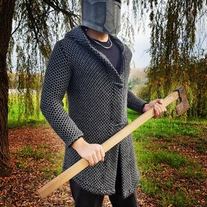 Finished leather Crusader Great Helm made from this DIY pattern. The helmet has a dark, weathered metallic finish designed to look like aged iron, worn by a person in chainmail armor holding a battle axe in a forest.
