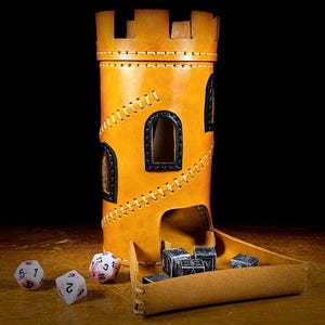 May include: A tan leather dice tower, resembling a castle, with black window frames and decorative stitching. The tower has a tray for dice to roll into, and several dice are scattered around it.