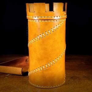 May include: A tan leather container, shaped like a castle tower, with a crenelated top. It has a spiral stitch design and a matching leather tray. The item is likely for storage or display. The measurements are in centimetres.
