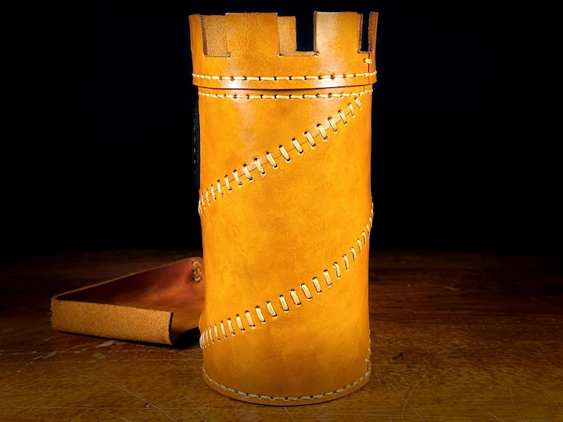 May include: A tan leather container, shaped like a castle tower, with a crenelated top. It has a spiral stitch design and a matching leather tray. The item is likely for storage or display. The measurements are in centimetres.