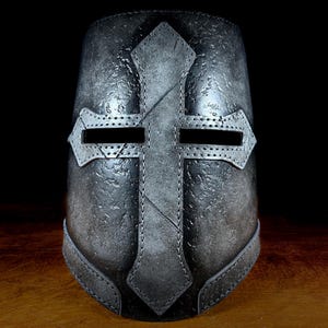 K&ouml;nnte beinhalten: Ein metallisch grauer Helm mit einem markanten Kreuzdesign. Der Helm hat eine genietete Kreuzform auf der Vorderseite, mit Augenschlitzen und einer strukturierten Oberfl&auml;che. Das Design deutet auf ein mittelalterliches oder historisches Thema hin.