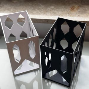 Könnte beinhalten: Zwei geometrische Aufbewahrungsboxen, eine weiße und eine schwarze, mit einem Wabenmuster. Die Boxen sind aus leichtem Material gefertigt und haben ein modernes Design.